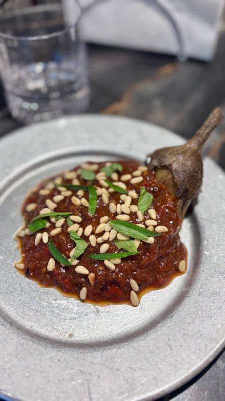 Тарелка с печёным баклажаном в соусе с кедровыми орехами и яркой островатой сальсой — крупный план блюда на мраморном столе.