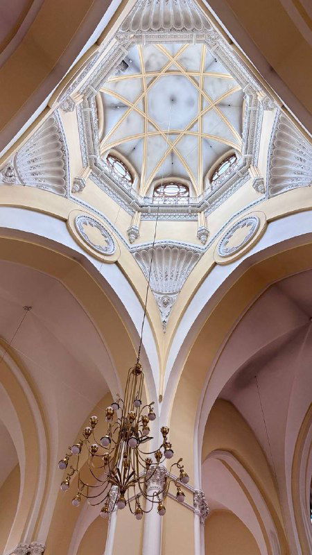 Вид вверх на декоративный купол и перекрытия интерьера собора: позолоченные детали, своды и центральная люстра в нефе католического храма.