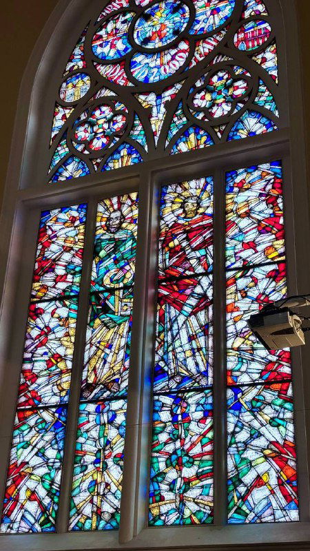Большой витраж с яркими цветными фрагментами в одном из окон собора: стеклянная композиция добавляет света и художественной детали интерьеру.