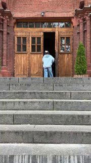 Подход к входу собора: широкая лестница, человек поднимается к деревянной двери, акцент на масштабе и доступности входной группы храма.