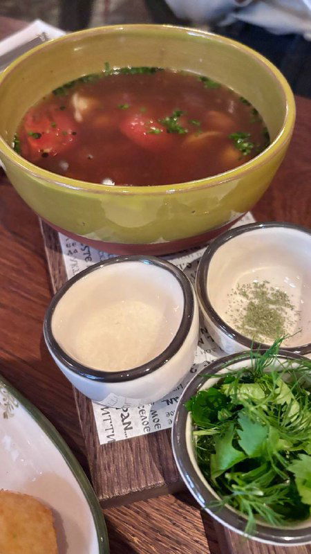 Чаша с азербайджанским супом дюшбара, рядом маленькие пиалы с приправами и зеленью — традиционная подача супа.