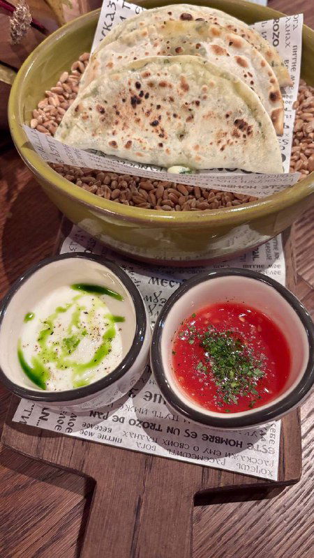 Тарелка с кутабы и несколько соусов в маленьких мисках: творог, зелень и томатный соус — акцент на многообразии вкусов.