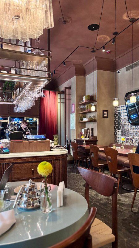 Общий вид зала бистро с барной стойкой, столиками и источниками света — тёплая, гостеприимная обстановка для гурманов.