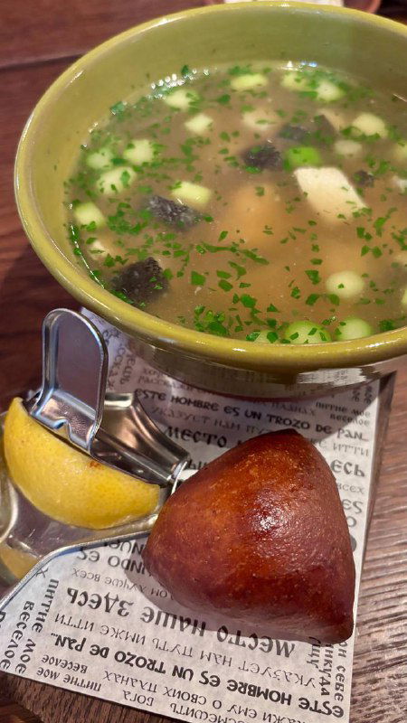 Чаша прозрачного супа с кусочками мяса или рыбы, долька лимона и поданная булочка — подача традиционного первого блюда.