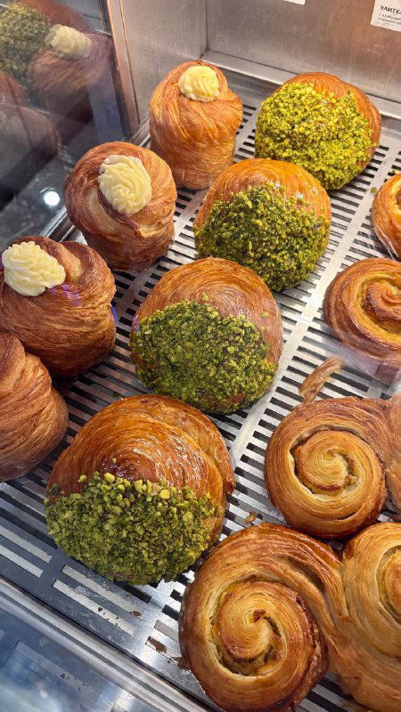 Витрина с булочками: даниши, круассаны и изделия с фисташковой посыпкой и кремовыми начинками — выпечка выложена на решётке кафе.