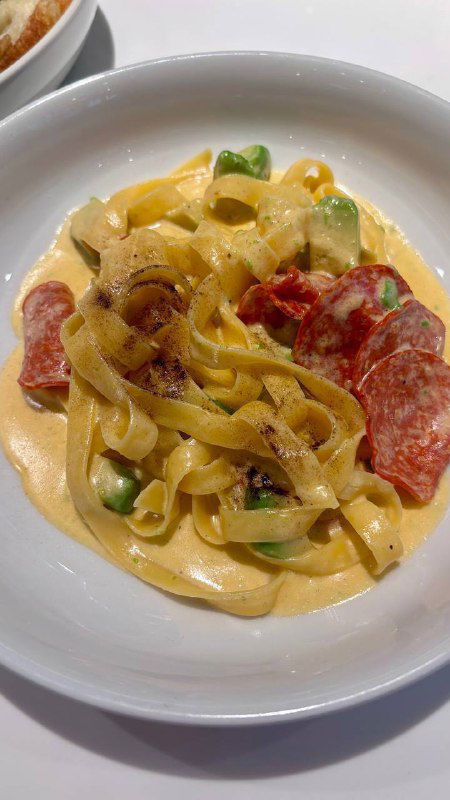 Паста или тёплое блюдо с широкими лентами пасты, кусочками колбасы и кремовым соусом — подача выглядит густой и насыщенной.