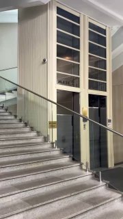 Лестничная площадка внутри Наркомзема с видимыми дверцами и корпусом единственного лифта‑патерностера, перила и мраморные ступени на переднем плане.