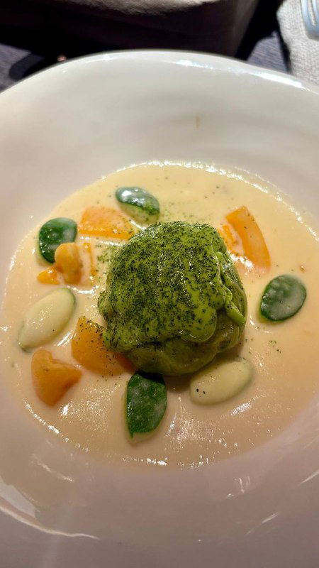 Деталь блюда с зеленым овощным элементом на кремовой подложке, бобы и кусочки тыквы — интерьерный кадр блюда в ресторане.