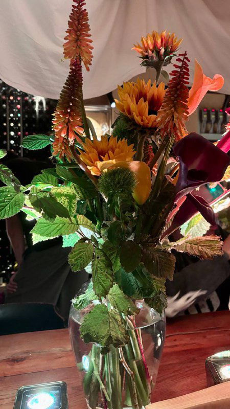 Высокая интерьерная композиция из подсолнухов и декоративных цветов в вазе на столе ресторана — элемент оформления пространства.