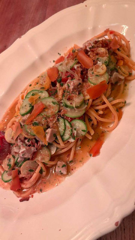 Спагетти с тунцом и овощными лентами в сливочном соусе, подача на длинной белой тарелке — вид сбоку.