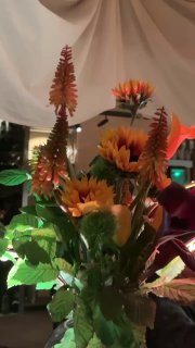 Крупный план букета с высокими оранжевыми цветами и подсолнухами в вазе на столе — декоративный акцент интерьера.