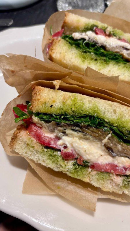 Сочное фото сендвича с баклажаном, песто и зеленью в бумажной упаковке — крупный кадр с текстурой хлеба и начинкой, на тарелке.