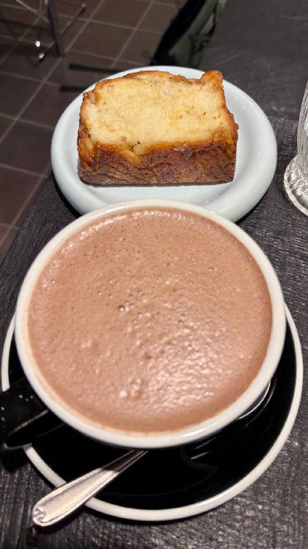 Чашка горячего напитка и кусочек кекса или бабки на блюдце — сочетание выпечки и кофе в минималистичной подаче внутри пекарни.