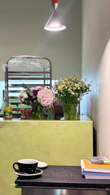 Интерьер пекарни Loave: прилавок с цветами и лампой, столик с чашкой — светлая уютная зона внутри заведения рядом с витриной.