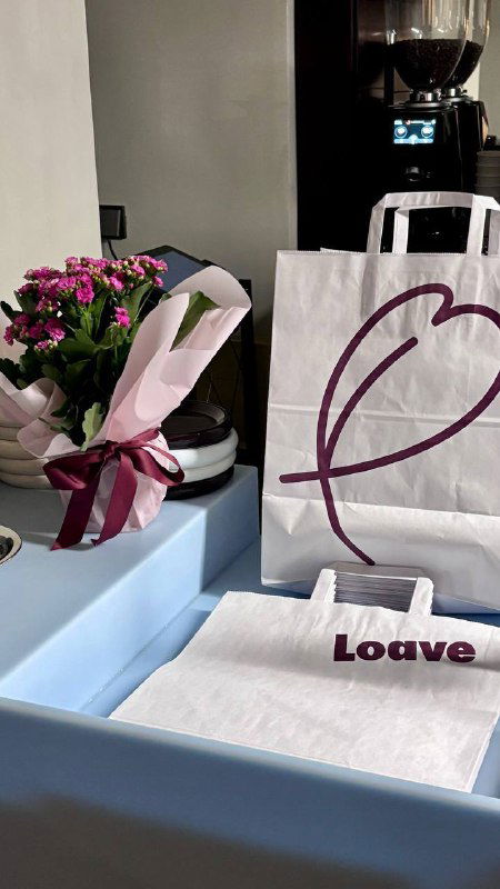 Пакеты и элементы фирменной упаковки Loave на прилавке: бумажные пакеты, цветы и минималистичная брендированная подача.