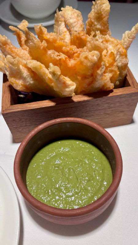 Хрустящие жареные цветы цукини в деревянном ящике, перед ними миска с ярко-зелёным соусом — закуска и акцент подачи в Luigi`s garden, Москва.