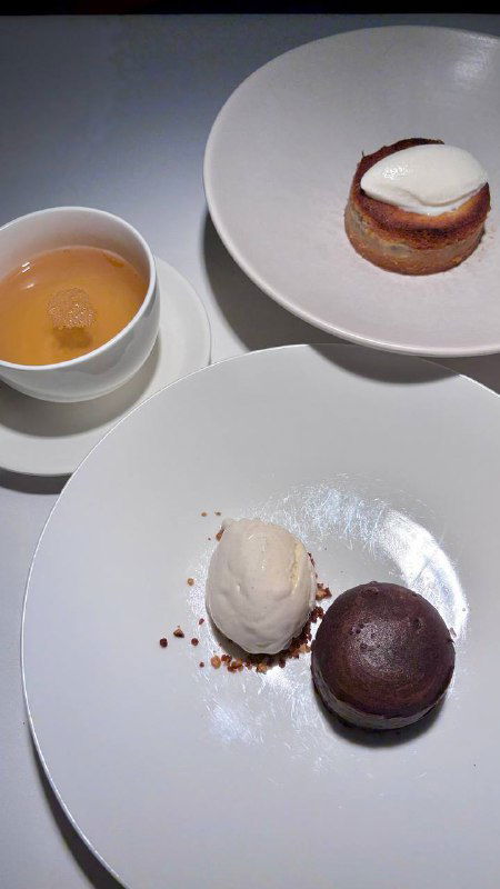 Три десерта на белых тарелках: фондан, шар мороженого и мини-пирожное рядом с чашкой — сладкая часть дегустации в ресторане.