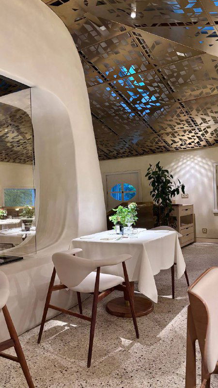 Интерьер ресторана: пустой столик с белой скатертью, дизайнерский перфорированный потолок и сдержанная цветовая гамма — атмосфера зала Luigi`s garden.