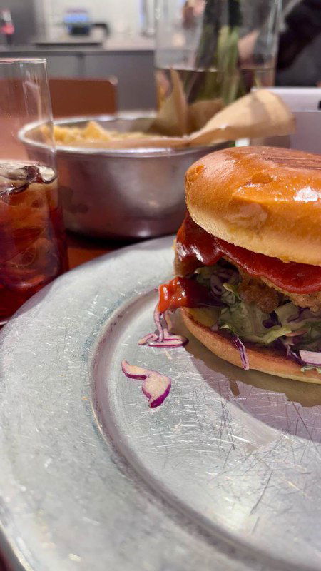 Бургер на тарелке вблизи, виден расплавленный сыр, салат и соус, рядом кадр с сервировкой и корзиной для картофеля.