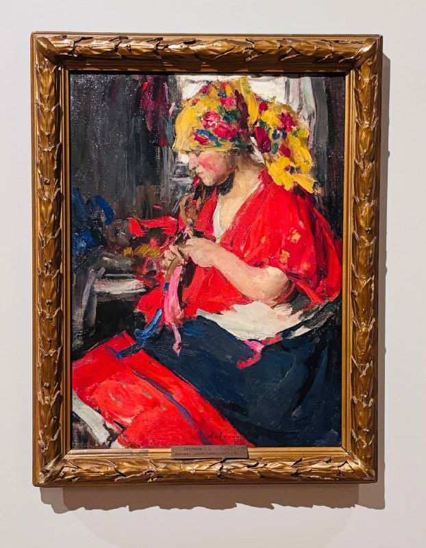 Женщина в красной рубашке и цветочном платке, занятая рукоделием; живописная фактура и золочёная рама, характерная для экспозиции.