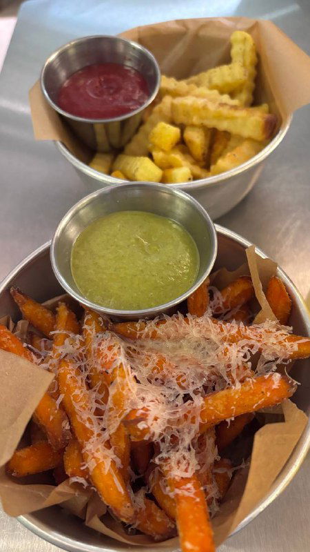 Две порции картошки фри в металлических стаканчиках: классическая и сладкая, одна присыпана сыром, рядом соус в металлической чашке.