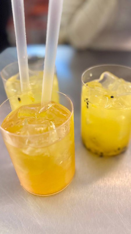 Стаканы с яркими желто-оранжевыми коктейлями из цитрусовых на столе; на заднем плане размытые элементы интерьера кафе.