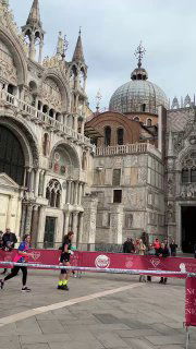 Бегуны преодолевают дистанцию на площади Сан‑Марко на фоне величественного собора; спортивное событие на историческом фоне Венеции.