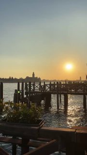 Романтический закат над венецианской лагуной: солнце низко над горизонтом, деревянный пирс и отражения в воде, тёплая вечерняя палитра.