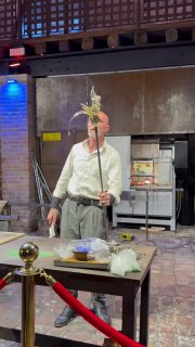 Мастер держит заготовку на металлическом жезле и показывает её посетителям, отображая процесс создания муранского стекла и демонстрацию для туристов.