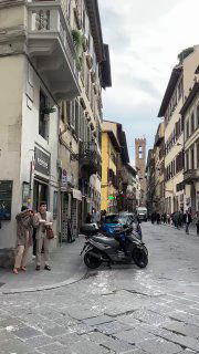 Узкая флорентийская улица с припаркованными мотоциклами, пешеходами и классическими фасадами — повседневная уличная сцена города.