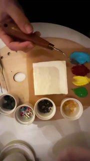 Рука держит скребок над квадратным тортом на палитре; вокруг мисочки с красками, ягодами и инструментами для украшения и росписи.