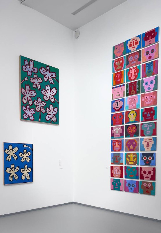 Угловая экспозиция с крупными яркими картинами и сеткой из маленьких квадратных портретов на белой стене в музее, художественный стенд в МАММ.