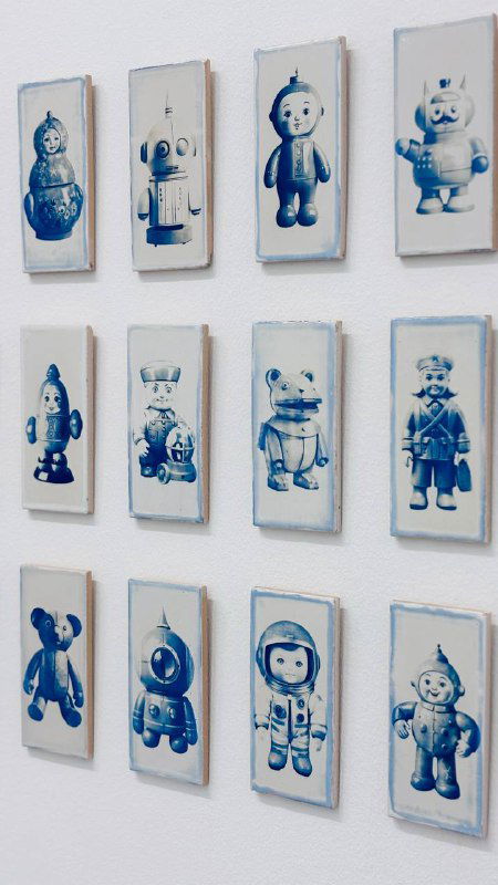 Стена с маленькими рамками, в каждой изображён ретро-персонаж или игрушечный силуэт, аккуратно выстроенные в сетку в экспозиции музея современного искусства.