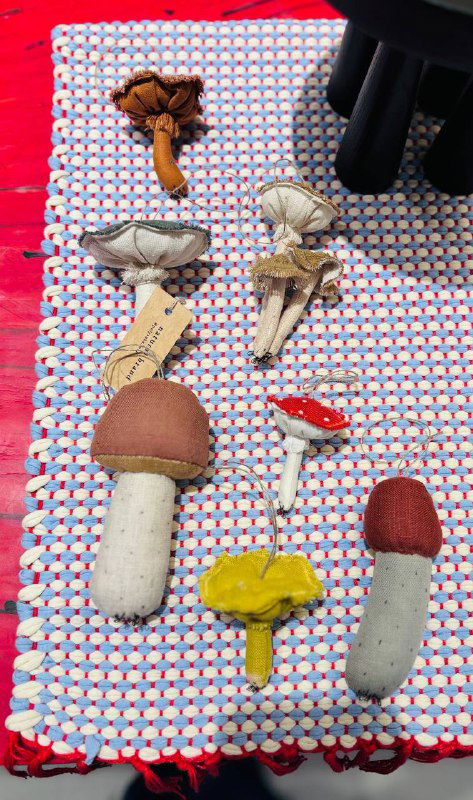 Крупный план текстильной поверхности с маленькими декоративными брелочками‑грибами, аккуратно выставленными на цветном коврике внутри магазина.