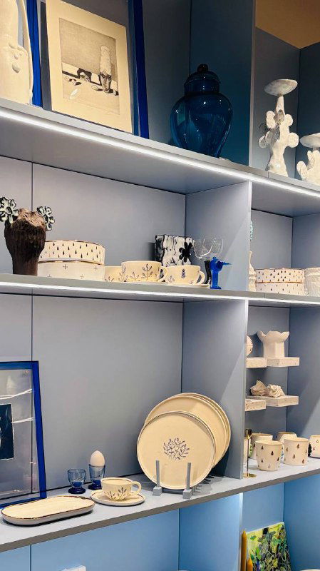 Пастельные полки с фарфоровыми и керамическими предметами: тарелки и чашки аккуратно расставлены в светлой витрине магазина Локалы.
