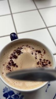 Крупный план напитка «Леччезе» — тёмно-коричневая посыпка на взбитой пенке эспрессо с миндальным молоком, ложка спереди