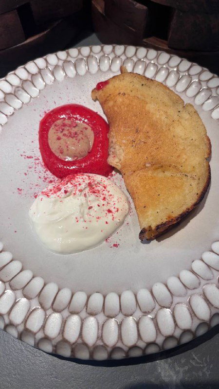 Блин из печи на белой тарелке с соусом и сливочным кремом, рядом розовое пюре или ягодный акцент, текстура и сервировка.