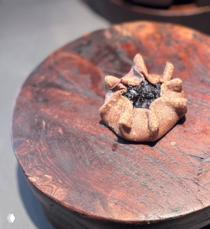 Карельская калитка на деревянной подставке: ржаной открытый пирожок с тёмной начинкой, крупный план и естественное освещение.