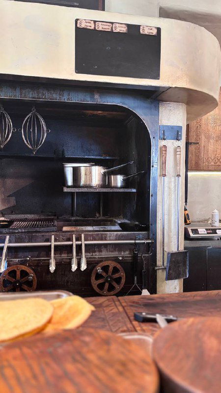 Пекарская печь и рабочая зона кухни ресторана: кастрюли, духовка и деревянные поверхности, вид с барной стойки.