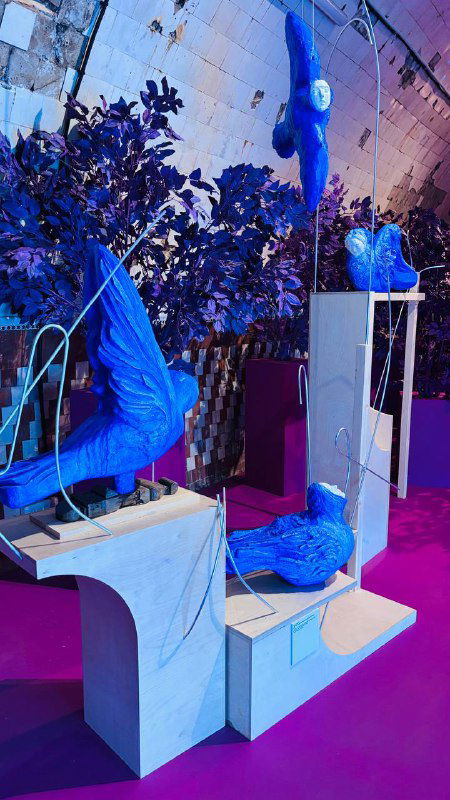 Композиция с синими скульптурными фигурами и архитектурными элементами на цветном подиуме — современный сценографический приём.