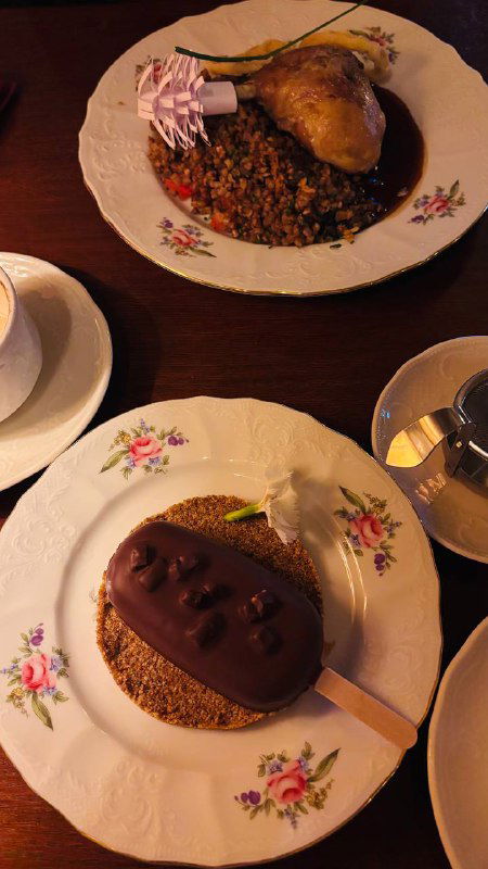 Тарелка с утиной ножкой и гречневой кашей на фарфоре в элегантной подаче, рядом кофейная чашка и приборы в ресторане «Пушкинъ».