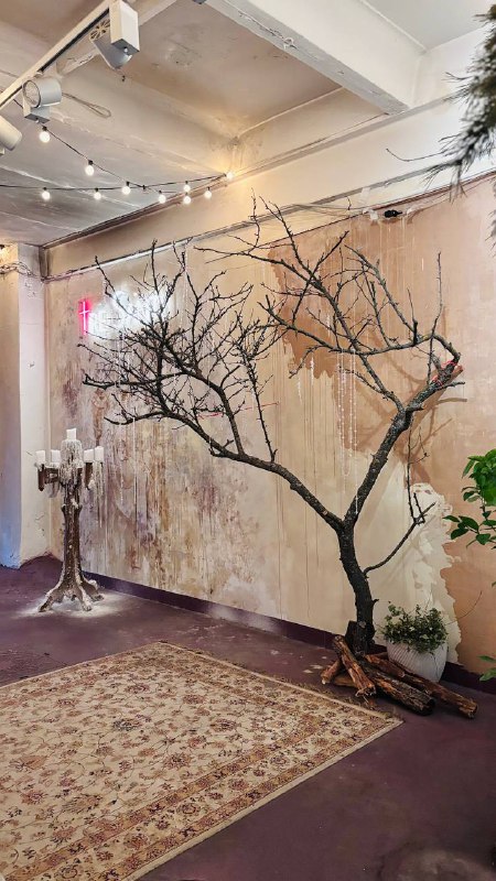 Интерьер ресторана с декоративным голым деревом у стены, ковром на полу и мягким художественным освещением в уютном зале