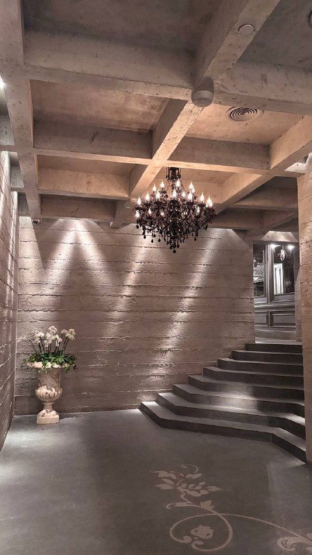 Лестничная зона внутри Шануар: ступени, бетонные потолки и сдержанная подсветка, интерьер с цветочной композицией у стены и атмосферой премиума.