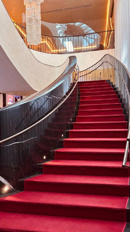 Внутренняя изящная лестница с красным ковровым покрытием и балюстрадой, создающая эффект ретро‑гламура в интерьере старого московского кинотеатра.