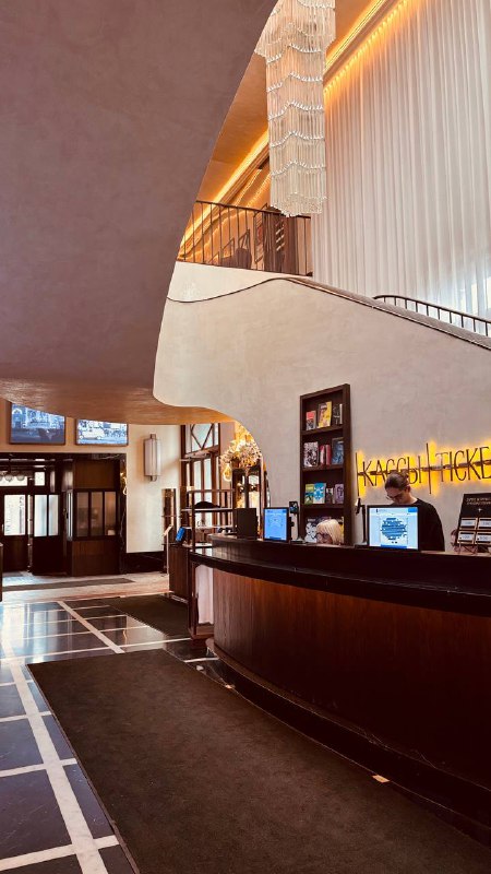 Уголок лобби с ресепшеном и полукруглой барной стойкой, полками с изданиями и тёплым освещением, характерным для исторических кинотеатров Москвы.