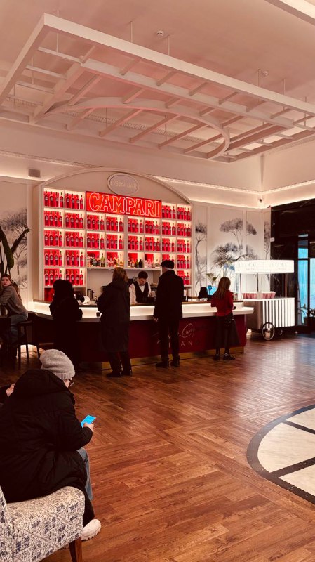 Барная зона с посетителями у стойки, деревянный паркет и полки с предметами декора, создающие живую атмосферу перед сеансом в «Художественном».