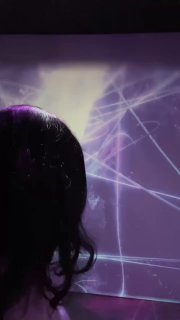 Силуэт посетителя на фоне фиолетовой проекции: светящиеся пересекающиеся линии и геометрические узоры иммерсивной инсталляции в зале.