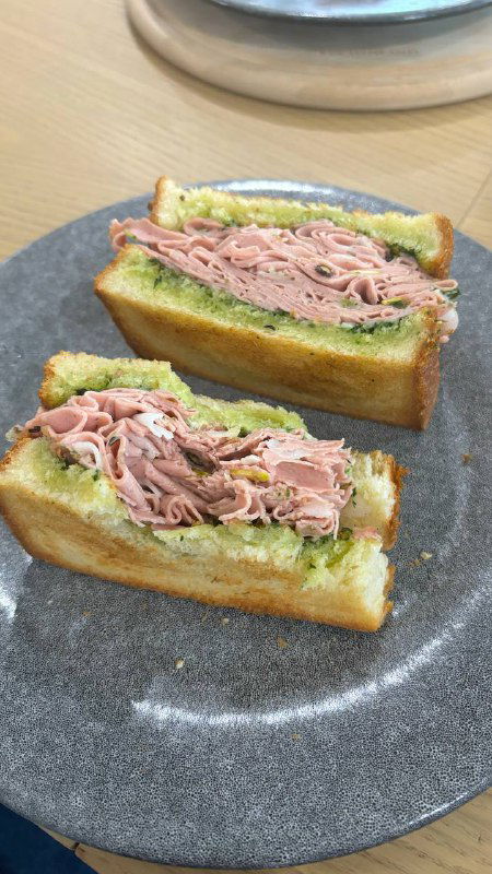 Разрезанный сэндвич с мартонадой или мартаделой, слои мяса и поджаренного хлеба хорошо видны на серой тарелке, минималистичная подача.