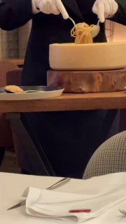 Подача спагетти cacio e pepe в сырной головке: повар извлекает пасту из пармезановой головы у стола, демонстрация подачи блюда в ресторане.