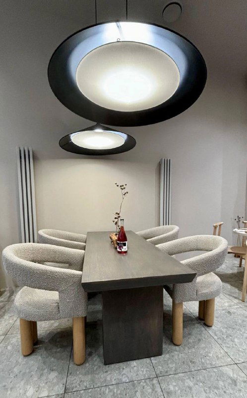 Интерьер ресторана: деревянный стол, мягкие светлые кресла и круглые подвесные светильники в минималистичном зале — атмосферный кадр из заведения.